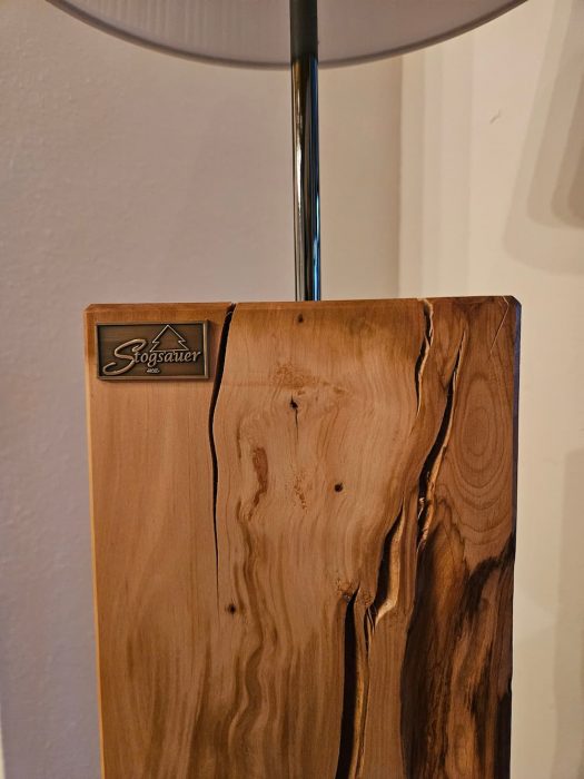Detailaufnahme einer Stehlampe aus Nussbaum mit ausdrucksstarker Maserung und Stogsauer Hoiz Logo